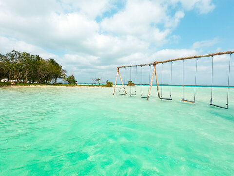 View of Bacalar Lagoon with wooden swings suspended over the clear turquoise water, surrounded by lush trees under a bright blue sky in Quintana Roo, Mexico.