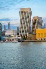 Fototapeta premium Two angled towers rise above the New York waterfront.. Brown window grids stand beside a yellow building with blue water across the vertical foreground.