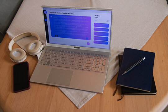 Silver laptop is showing digital marketing interface on light wood table with headphones, notebooks