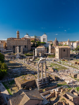 View of the ancient ruins of the Roman Forum with the Temple of Castor and Pollux and the Arch of Septimius Severus under a clear blue sky in Rome, Lazio, Italy.
