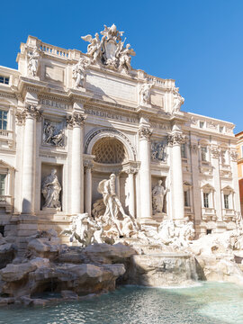 View of the Trevi Fountain with its intricate baroque sculptures, cascading water, and ornate facade under a clear blue sky in Rome, Lazio, Italy.