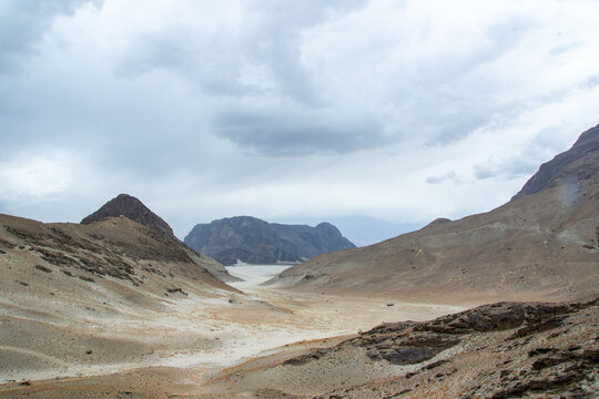 View of the arid landscape of Shigar Valley with rugged mountains and a sandy valley floor under an overcast sky in Shigar, Gilgit, Pakistan.