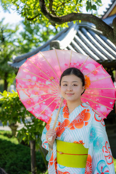 A young Japanese woman wearing a colorful floral yukata holds a cherry blossom parasol in a traditional garden in Senso-ji Temple, Tokyo, Japan, showcasing culture.