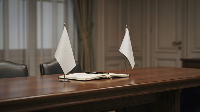 Business conference room with a wooden table, flags, an open notebook, and pens, representing diplomacy or corporate meetings