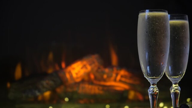 Champagne flute set against the warm, flickering glow of dancing flames in a fireplace. Intimate cozy and romantic evening for two, relaxed and luxurious atmosphere. Rich amber tones  enhance the sens