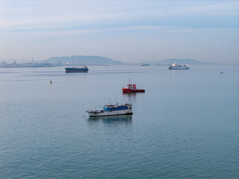 Penang, Malaysia - 10 June 2026: Aerial view of various cargo ships and small fishing boats anchored in the calm waters of the Penang Strait under a clear sky.