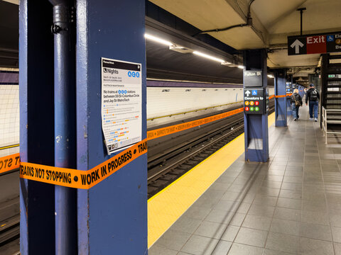 New York, USA, 1 Jule 2026 : Warning tape crosses a platform at Fulton Street subway station.. Blue columns flank tracks beside a yellow edge under ceiling lights with passengers farther away.