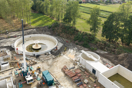 Diepenbeek, Flanders, Belgium - 30 August 2026: Aerial view of a wastewater treatment plant construction site featuring large circular concrete settling tanks and a mobile crane.