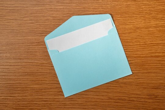 Open blue envelope with a blank white paper card inside on a wooden table. Mail, invitation, letter, newsletter, or business contact concept. Copy space for text.