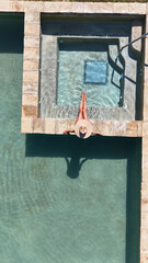 Aerial view of a woman relaxing in a stone-lined resort hot tub with turquoise water