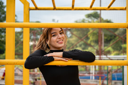 Colombian teen girl posing playfully on monkey bars at an outdoor park, showing a youthful and active lifestyle during a day of recreation and fitness