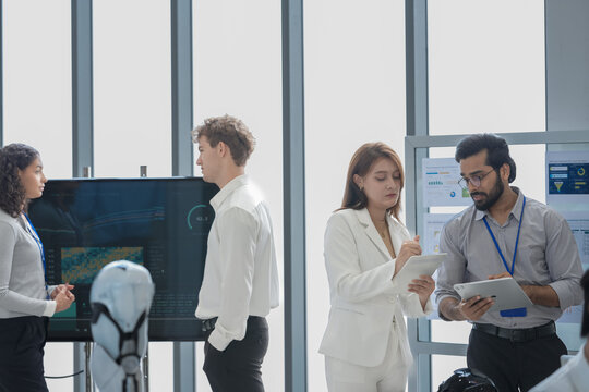 Wide view of a bright tech office where engineers review chip data on a large screen and tablets beside a humanoid robot, during an iterative design check, a digital transformation concept