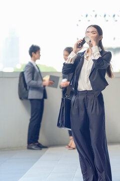A young female executive with long dark hair checking messages on a smartphone with coffee in hand on a skywalk above the business district, showing how work happens beyond the meeting room