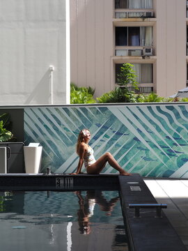 Woman sunbathing next to a teal geometric tiled wall at a hotel swimming pool