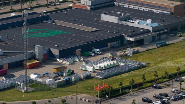 Duiven, Gelderland, Netherlands - 16 June 2026: Aerial view of the Volta Energy facility, featuring rows of mobile solar-powered generators parked in the yard next to an industrial building.