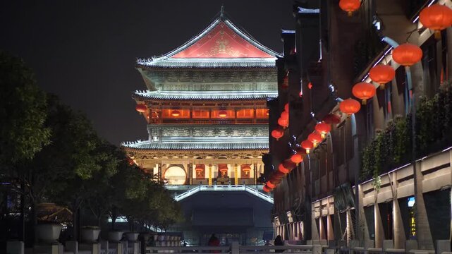 Illuminated traditional Chinese bell tower at night with glowing red lanterns and golden roof, historic city landmark in, night market