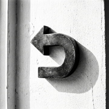 Artistic black and white shot of a metallic U-turn arrow mounted on a wall with deep shadows and industrial texture.