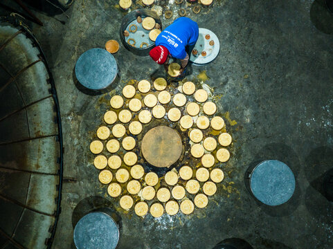 Bogura, Bangladesh - 14 December 2024: Aerial view of a worker arranging small bowls of curd in a circular pattern on a factory floor.