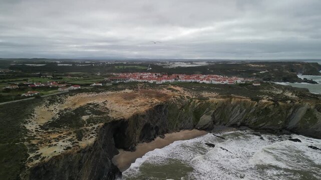 Aerial view of the coastal town of Zambujeira do Mar with rugged cliffs and sandy beach in Zambujeira do Mar, Beja District, Portugal.