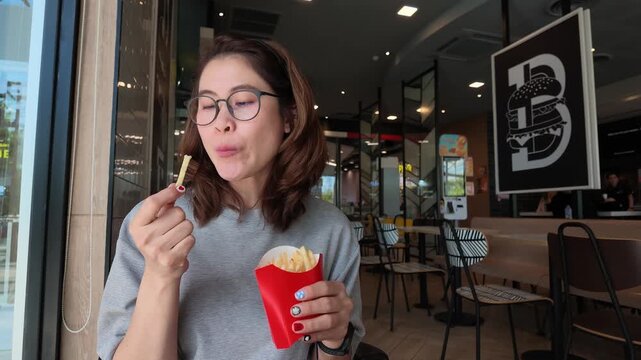 Asian woman eating french fries in cafe shop. French fries are long, thin strips of potato that are deep-fried or baked until crispy