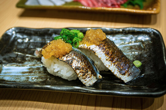 Closeup of Aburi Iwashi nigiri sushi, which is flame-seared Japanese sardine sushi served over seasoned sushi rice with grated daikon and spring onions. 