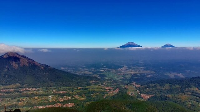 Aerial view of Pagergunung mountain landscape with lush green slopes and distant volcanic peaks above clouds in Ngablak, Central Java, Indonesia.