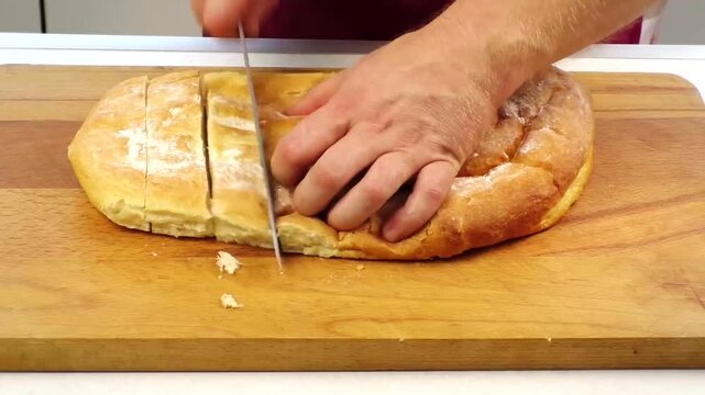 Freshly baked artisan bread being sliced on wooden cutting board with chef's knife