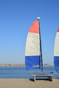 Hobie cat catamaran sailboat with red white and blue sails on sandy beach of Mission Bay San Diego, California