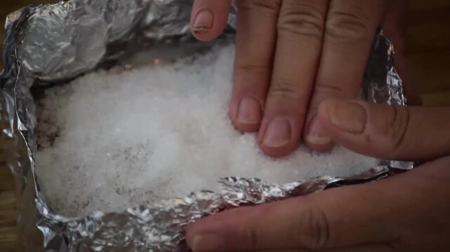 Hand pressing coarse salt onto food inside a foil packet during cooking preparation