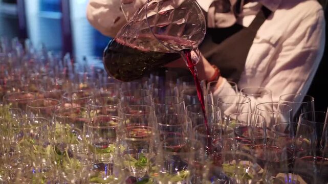 Waiter pouring red wine from a crystal decanter into rows of glasses at a formal event