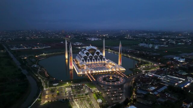 Aerial view of Al Jabbar Grand Mosque at night with illuminated minarets and reflection in the surrounding water in Bandung, West Java, Indonesia.
