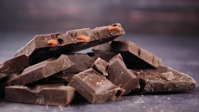 Dark chocolate pieces stacked on a dark surface with pieces broken off