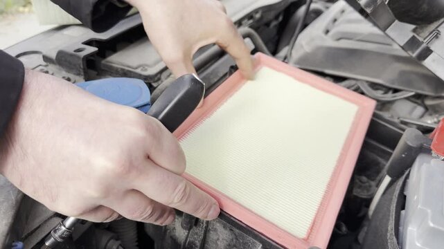 A man is changing the air filter in a car. Close-up.