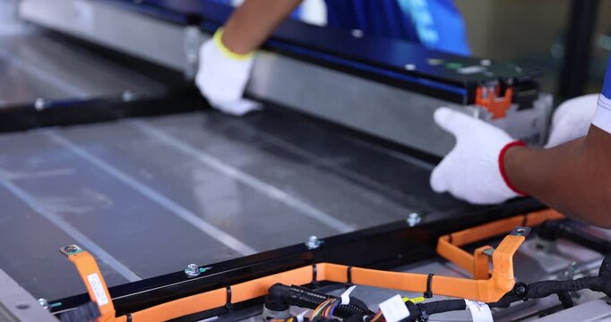 Close-up of technicians wearing white gloves lifting and positioning a long electric vehicle battery module inside an open pack housing.