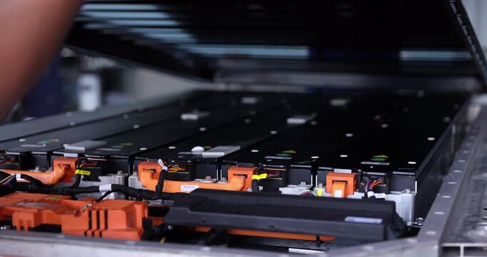 Technicians wearing gloves work together to lower a cover onto an electric vehicle battery pack.