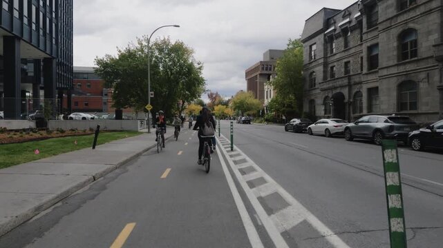 First person ride on an electric shared bike along a protected bike lane with green bollards in a leafy Montreal neighborhood with natural sound on a cloudy day