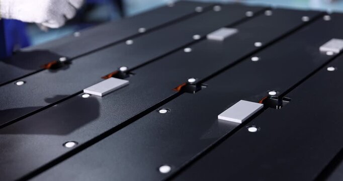 Close-up of a gloved technician using a hand tool to install fasteners on electric vehicle battery modules in preparation for assembly. 