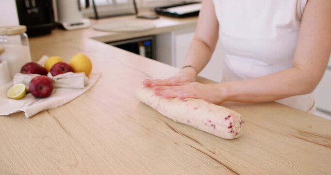 Baking process. Rolling dough. Female confectioner hand shaping sweet treat log on wooden counter preparing biscotti with red berry.