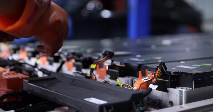 Close-up of a technician wearing orange gloves handling multipin wiring harness connectors inside an electric vehicle battery pack.