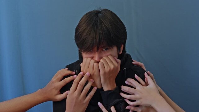 Frightened young asian man biting nails and multiple hands reach in to grab and touch him for bipolar concept
