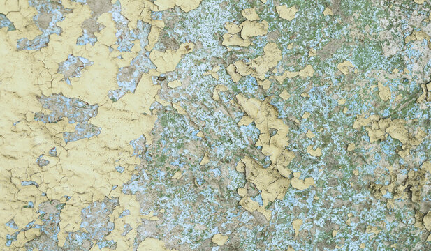 Texture background with peeling yellow paint over older blue and green layers and a mottled weathered surface full of fine cracks