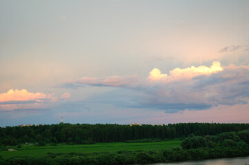 Nature landscape background, view from height at pink lit sunset clouds drifting over a dense green forest and a distant industrial chimney under a soft evening sky © syntheticmessiah