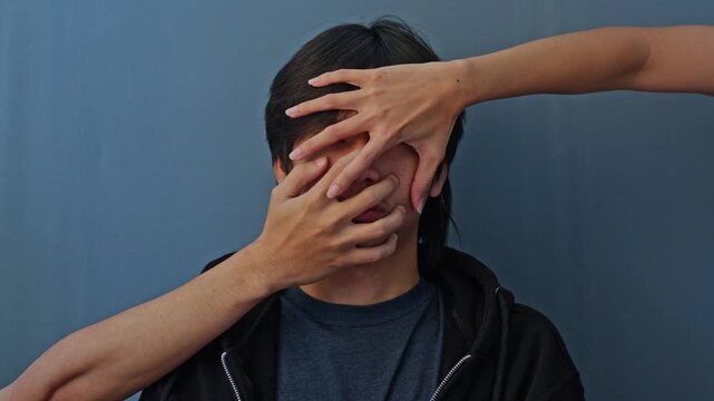 Young asian man face entirely covered and blocked by multiple hands symbolizing bipolar mental turmoil