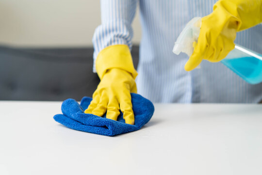 Close up of housekeeper in yellow gloves wiping table with microfiber cloth.