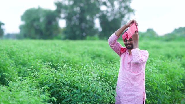 Happy indian farmer tying cloth or gamacha on head at agriculture field 