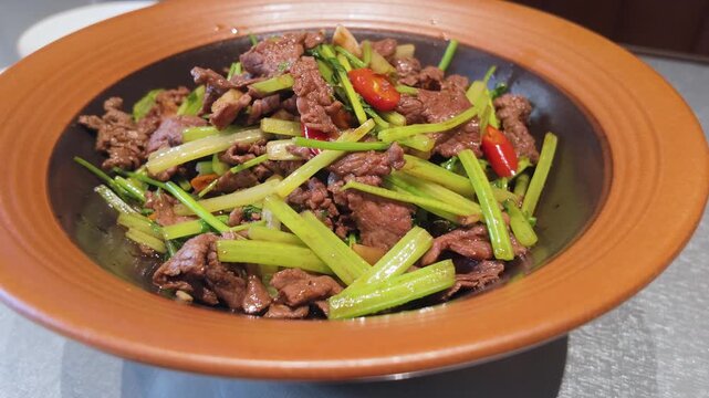 Chinese stir-fried beef with celery and red chilli in a rustic brown bowl, savory traditional home-style dish being served, close-up food footage