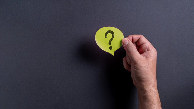 Male hand holding green speech bubble with question mark on dark background