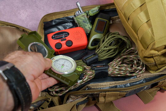 Man packing an emergency survival kit with various tools like a compass, radio, flashlight, and rope for outdoor adventure