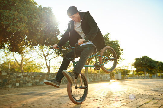 Urban, tricks and man on bicycle for cycling, training skill or sports in city to practice. Cool person, athlete or stunt biker in town at sunrise for endo, stoppie or outdoor activity for biking