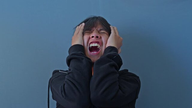 Young man grasps head and screams in agony and mental breakdown depicting severe bipolar disorder